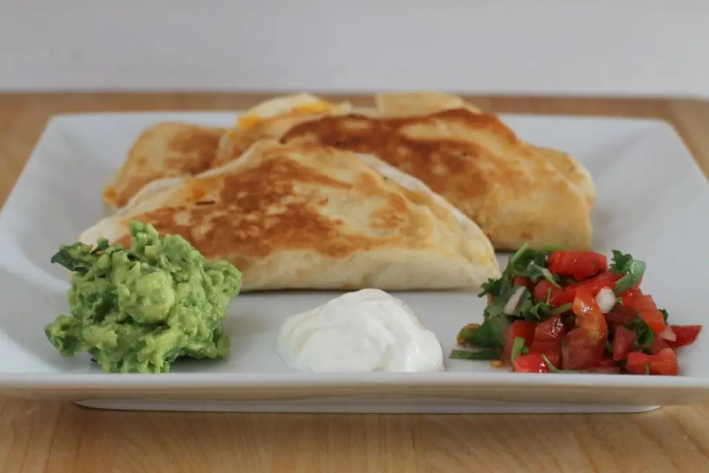 Two quesadillas on a white plate with guacamole and salsa.