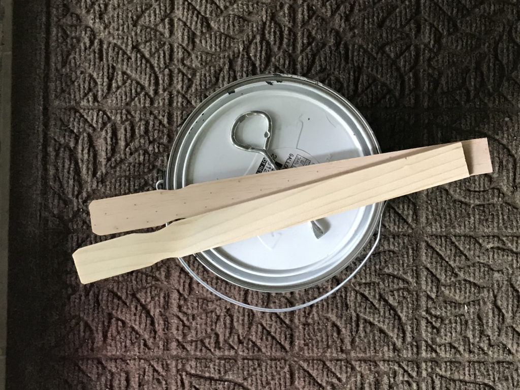 A bucket of paint with wooden stirring sticks on top of it.