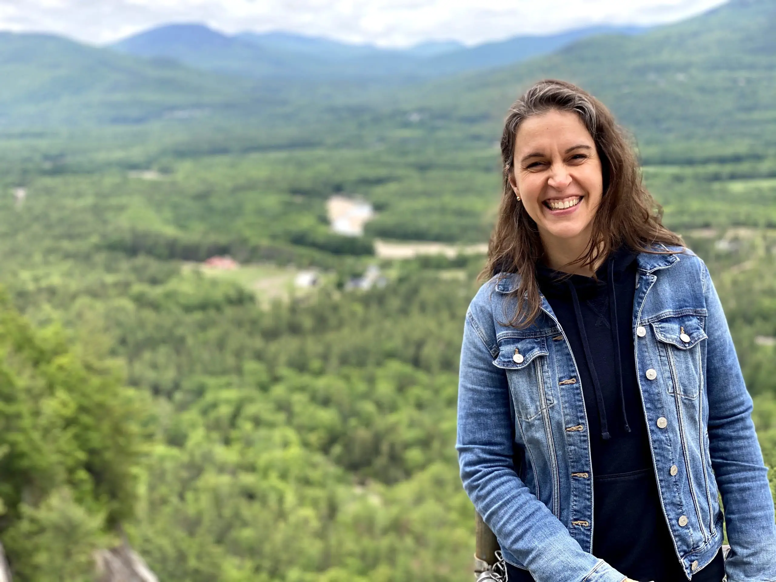 Kristen in front of a mountainous scene with green trees.