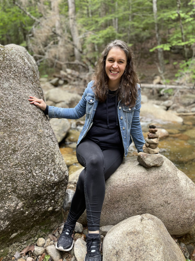 Kristen sitting next to a pile of rocks in the woods.